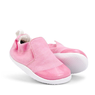 The Bobux Xplorer Scamp Crawler Candy Pink 501707 Canvas toddler shoes feature a flexible sole, white trim, soft fabric, and a pull tab at the heel, shown against a white background.
