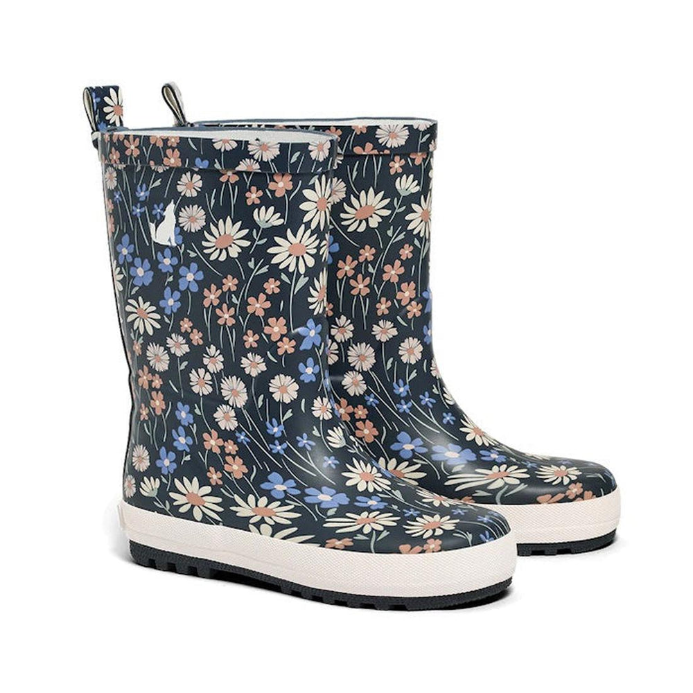 A pair of CryWolf Rain Boots in the Winter Floral Navy design is set against a dark background. These children’s waterproof boots are made from natural rubber and feature a floral pattern with white, blue, and peach flowers. The thick white soles have black treads for extra grip.