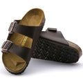 a pair of Birkenstock Arizona Smooth Leather Dark Brown Narrow Width with double straps, one over the foot and one over the toes with buckle adjustment. Staps are linked at the sides of the foot. Leather thick straps and a suede leather footbed. Also showing the left foot outsole lying down.,
