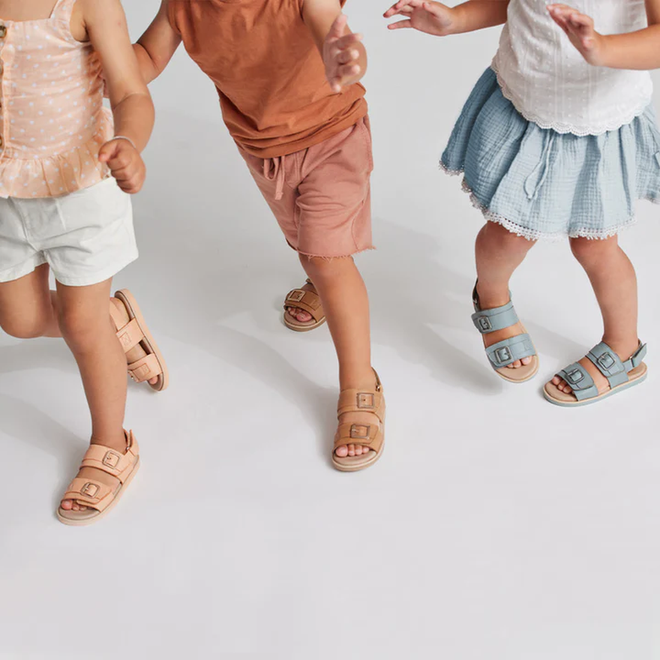 Three kids in summer outfits wear Pretty Brave Alex Leather Sandal Seaform Blue (sizes 29-33, clearance, not returnable) as they walk and play together on a white background, focusing on their legs and feet. Upper bodies mostly out of frame., 9421036357684, 9421036357691, 9421036357707, 9421036357714, 9421036357721