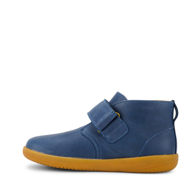 The Bobux Kid+ Desert Boot Midnight Blue 830312 is a children's unisex blue leather boot with a single Velcro strap, wide opening, and flat light brown rubber sole, displayed in profile on a white background., 9420068517035, 9420068517042, 9420068517059, 9420068517066, 19835, 19836, 19837
