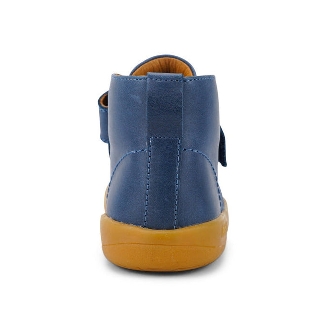 The Bobux Kid+ Desert Boot Midnight Blue 830312 is a blue high-top shoe with a tan rubber sole, seen from the back. It features a wide Velcro opening, vertical heel seam, and visible stitching details., 9420068517035, 9420068517042, 9420068517059, 9420068517066, 19835, 19836, 19837