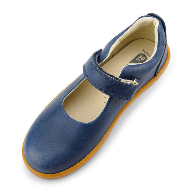The Bobux Kid+ Delight Mary Jane Navy 831615Z features a single blue shoe with a brown sole and Velcro strap, shown from an angled top view. Its rounded toe and cushioned beige interior are ideal for girls' leather school shoes., 9420075721210, 9420075721227, 9420075721234, 9420075721241, 9420075721258, 9420068516847, 9420068516854