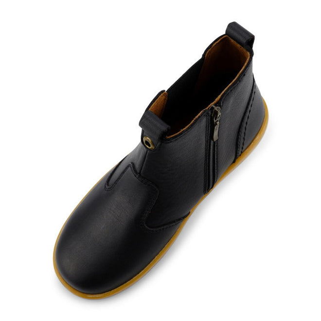 The Bobux Kid+ Jodphur Boot Black 830016Z is a unisex ankle boot in black leather with a tan rubber sole, brown lining, side zip closure, and front and back pull tabs, shown from an overhead angle., 9420075719811, 9420075719828, 9420075719835, 9420075719842, 9420075719859, 9420075719866, 9420075719873