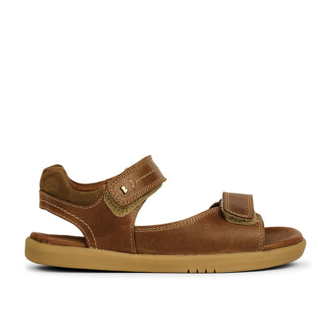 The Bobux Kid+ Plus Driftwood Caramel Open Toe Sandal 833504A features a brown leather upper, light tan sole, and adjustable double Velcro straps at the ankle and toes, shown in side profile against a white background., 9420062051078, 9420062051085, 9420062051092, 9420062051108, 9420062051115, 9420062051122, 9420062051139