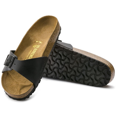 A pair of Birkenstock Madrid Womens Birko Flor Black Narrow Width sandals—one upright to show the top, the other flipped for the textured cork sole—crafted from durable Birko Flor material.