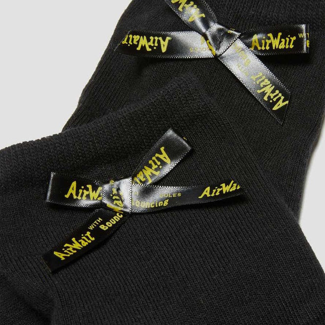 Close-up of Dr Martens Ankle Bow Cotton Blend Socks in black, featuring small black satin bows with yellow AirWair branding, ribbed texture, and overlapping display on a light background., 190665563641, 190665563634