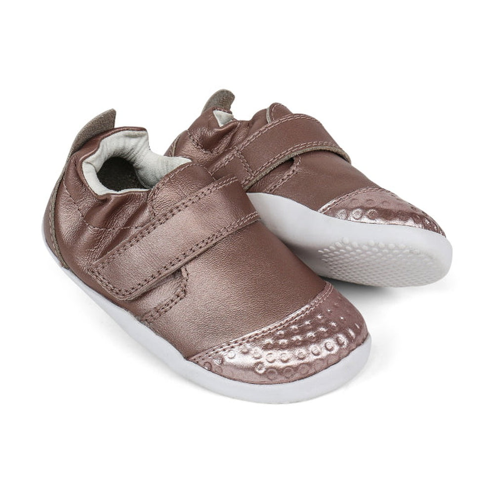 The Bobux Explorer Go Rose Gold First Walker Crawler 501015B features premium soft leather in metallic rose gold, velcro straps, white soles, and textured toe detailing, shown on a white background.