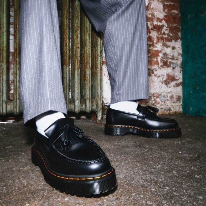 Someone stands before a distressed brick wall and old radiator, wearing Dr Martens Adrian Bex Black Smooth Platform Loafer Shoes (CLEARANCE), paired with white socks and gray pinstripe trousers., 183681, 190665420241, 190665420166, 190665420173, 190665420180, 190665420197, 190665420203, 190665420210, 190665420227