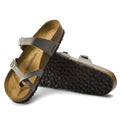 a pair of Birkenstock Mayari Birko Flor Birkibuc Earthy Stone Regular Width- thin strappy sandals with bubkle adjustment over the foot and on the outside of the foot near the toe area. Straps cross cross over the toes and a separate strap over the top of the foot. Suede foot bed with arch support. Mostly a women's styel
