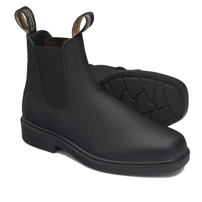 A pair of Blundstone 063 Dress Chelsea Boots in black leather with chisel toes and pull tabs is shown on a white background. One boot stands upright and the other lies on its side, showcasing the textured sole. Suitable for both women and men.