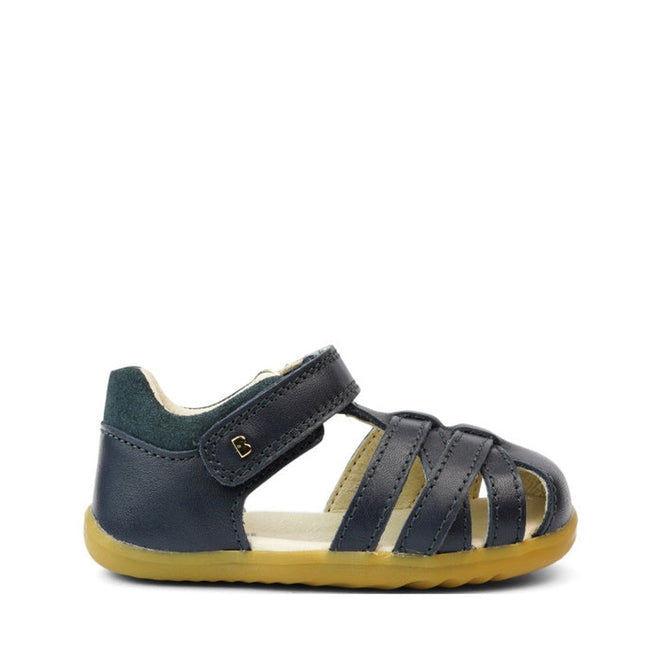 The Bobux Step Ups Cross Jump Navy Closed Toe Sandal is a unisex kids' sandal in navy leather with a closed heel, open toe, velcro strap, and flexible light brown sole—ideal as a first walker and shown on a white background., 9420062083567, 9420062083574, 9420062083581, 9420062083598