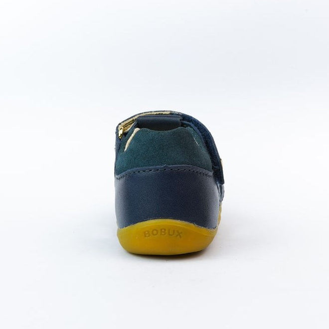 A single small Bobux Step Ups Cross Jump Navy Closed Toe Sandal is shown from the back, featuring dark blue leather and green suede upper, a yellow rubber sole, and "BOBUX" embossed on the heel. The background is plain white., 9420062083567, 9420062083574, 9420062083581, 9420062083598