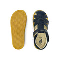 The Bobux iwalk Cross Jump Sandal Navy Closed Toe 636703 is shown: one sandal displays crisscross straps and a buckle from the top, the other highlights the tan textured sole from the bottom., 9420062083604, 9420062083611, 9420062083628, 9420062083635, 9420062083642
