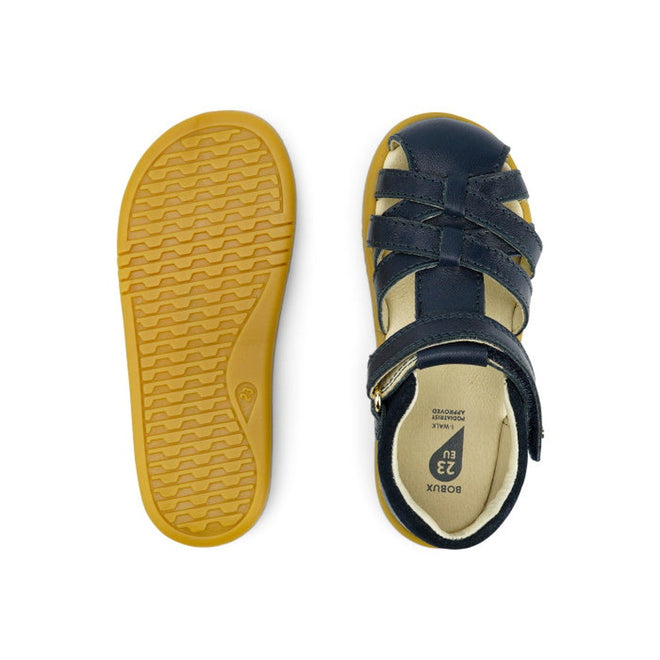 The Bobux iwalk Cross Jump Sandal Navy Closed Toe 636703 is shown: one sandal displays crisscross straps and a buckle from the top, the other highlights the tan textured sole from the bottom., 9420062083604, 9420062083611, 9420062083628, 9420062083635, 9420062083642