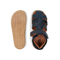 image of 2 bobux i-walk roam sandals in navy. 1 showing the sole ane the other a top down of the style showing the heel suport, protective toe covering an brown coloured foot bed. also shows the single velcro strap that fastens around the ankle.