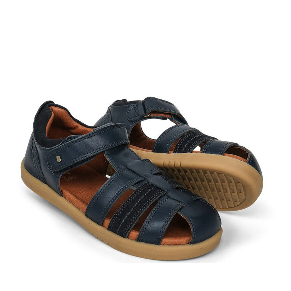 a pair of Bobux Kid+ Plus Roam Navy Closed Toe Sandal 830503A- closed toe sandals with closed back for heel support. velcro around the heel and straps of leather over the toes so air can move freely around the toes.