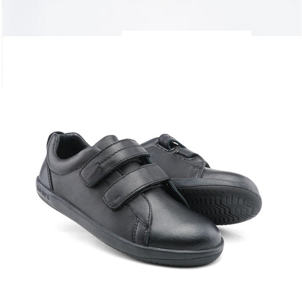 The Bobux Kid+ Black School Leather Shoe Venture Trainer is a low-top black sneaker with velcro straps and a non-marking rubber sole, shown on a white background.