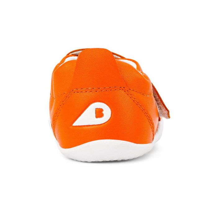 The Bobux Xplorer Go Tangelo First Walker 501035 is an orange baby shoe viewed from the back, made of soft leather with a white flexible sole and teardrop-shaped B logo on the heel, set against a plain white background., 9420071309429, 9420071309436, 9420071309443
