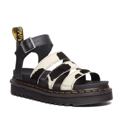 A side view of the outside of the right foot of aDR martens Blaire sandal with a black white cow print on hair over the 3 straps across the toes. a strap around the heel with buckle adjustment om a chunky sole
