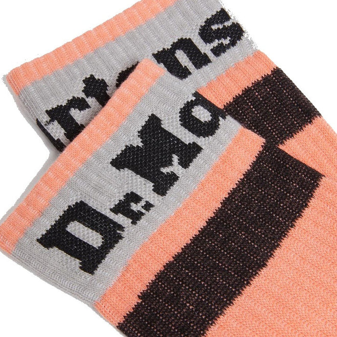 Close-up of two Dr Martens Organic Socks Athletic Logo Beige, machine washable, featuring peach, gray, and black horizontal stripes with bold black "De Mon" text partially visible., 190665558487, 190665558470