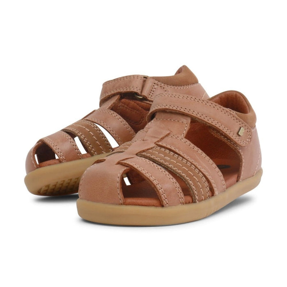 A pair of caramel tan bobux i walk sandals roam. angled to show the inside and outside of the feet and a small portion of the sole. Shows the toe covered with woven straps to allow are to circulate while still having protection. The heel supported and velcro fastening around the ankle.
