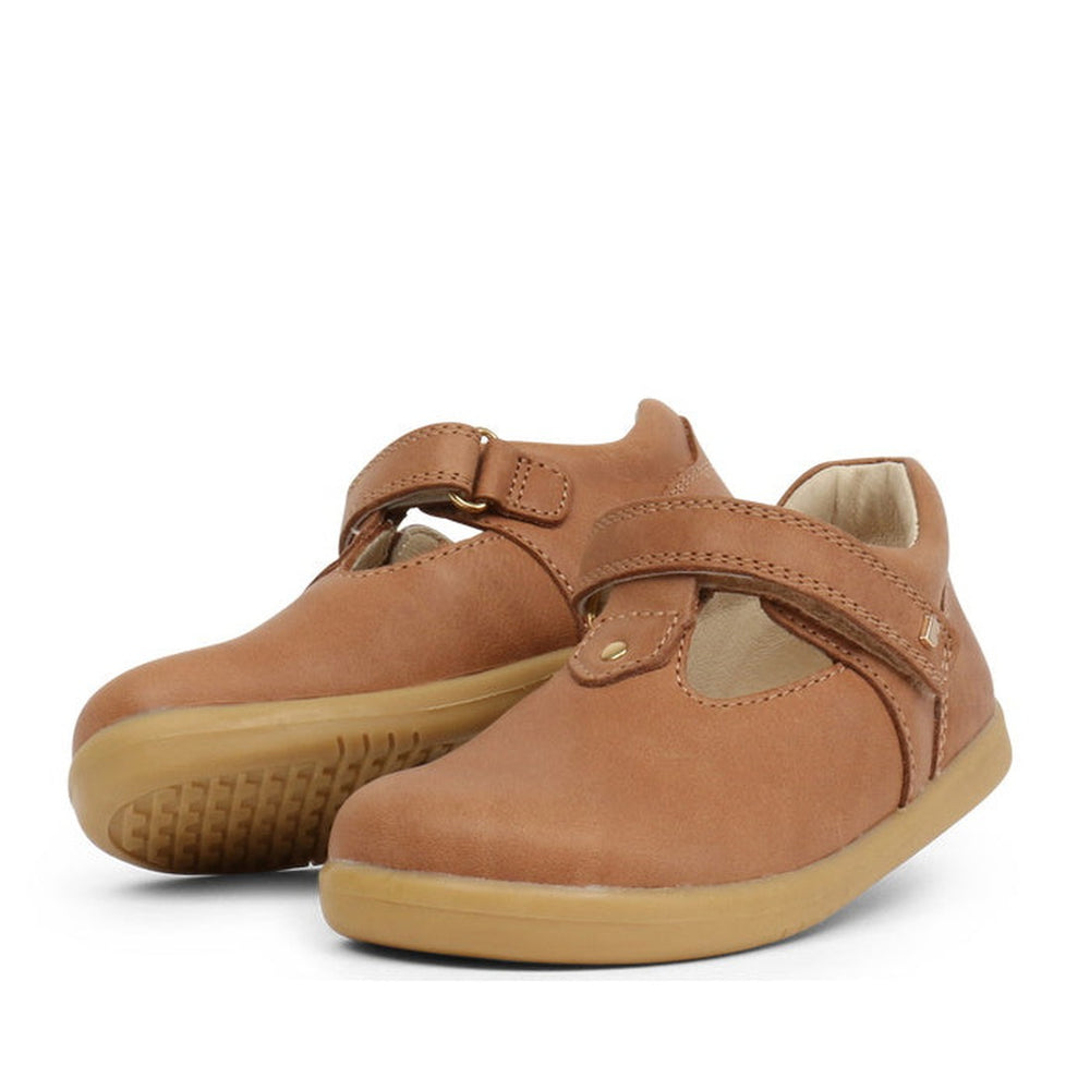 Bobux Iwalk IW Louise T-Bar Caramel Tan children's shoes with brown vintage leather, tan rubber soles, and adjustable straps are shown against a white background. One shoe stands upright while the other leans on its side.